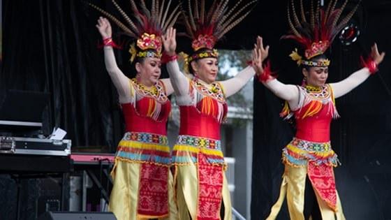 Three women dancing in colorful Indonesian feathered headdresses, yellow skirts, and beaded belts and collars.