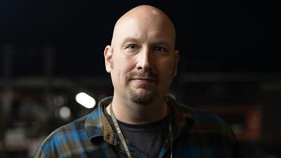 Headshot of Andrew Garraway wearing a blue and grey plaid flannel and a Full Sail lanyard, complete with Full Sail pins.