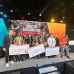 Techfest tournament winners holding large scholarship checks on stage alongside Full Sail staff members in the Fortress.